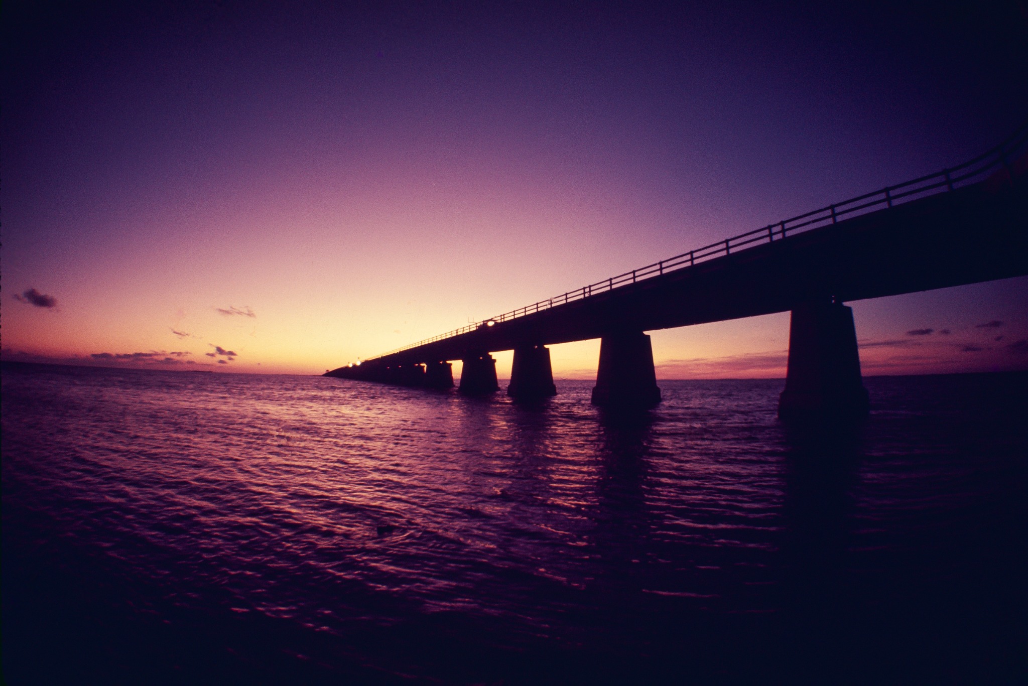 Long bridge silhouetted over the sea beneath a violet and orange sunset