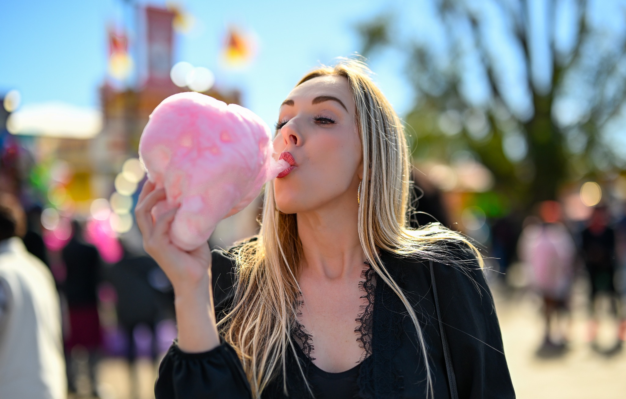 Woman enjoying pink cotton candy against a softly blurred, colorful fairground