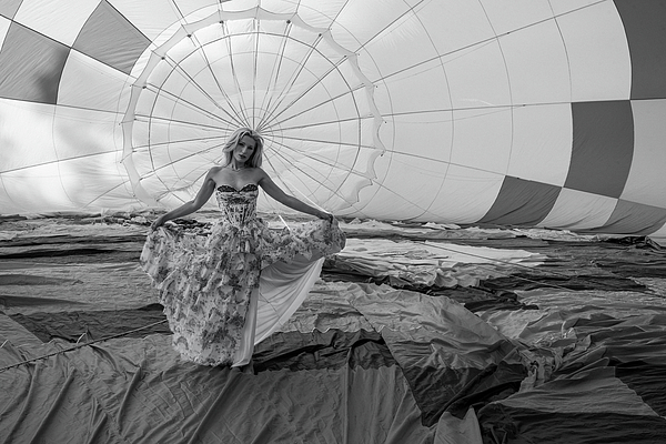 Black-and-white photograph of a woman holding out her floral dress inside a hot-air balloon